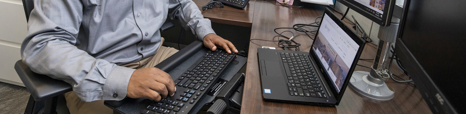 Photo of hands on a computer keyboard with a laptop sitting in front of it.