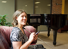 A blind woman sitting on a couch smiles as she listens to NFB-NEWSLINE on her phone.
